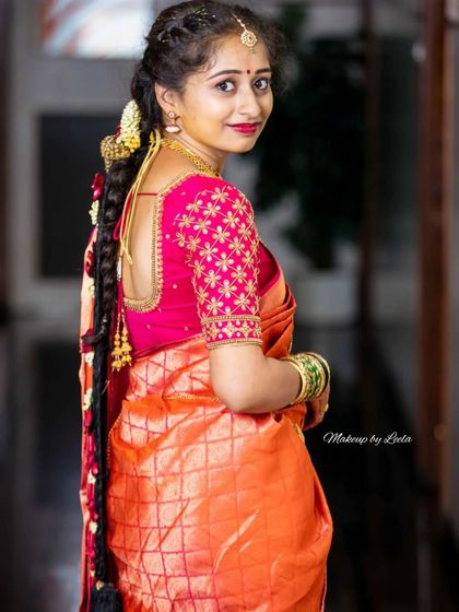 A view of the bride's complete look from the back, showing off her beautiful braided hairstyle with traditional gold accessories, complementing her orange Kanjeevaram saree.