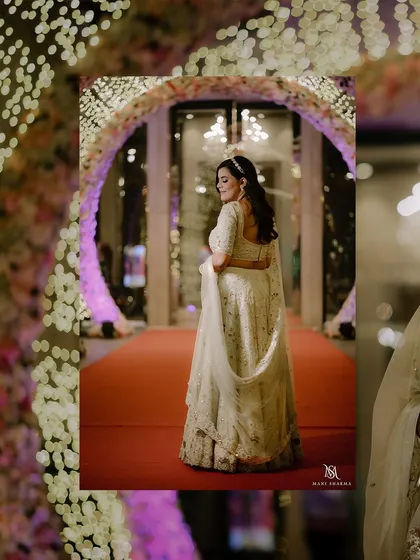 A full-length portrait of the bride on her engagement day, showcasing her elegant white lehenga against the red carpet. A classic and timeless shot.