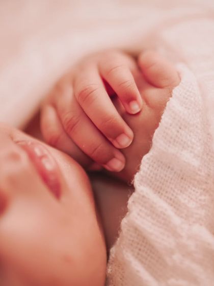 An extreme close-up of a newborn's hand resting by their face. This image is incredibly tender, focusing on the delicate skin and features of the baby.