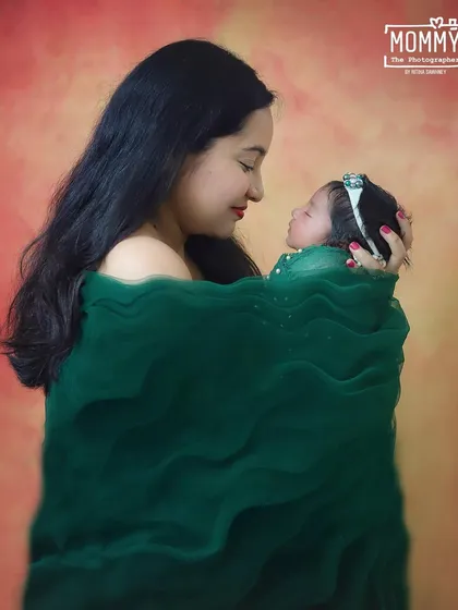 A mother gazes lovingly at her newborn, both wrapped in a beautiful green fabric. This simple, elegant portrait focuses entirely on their connection and the quiet joy of motherhood.