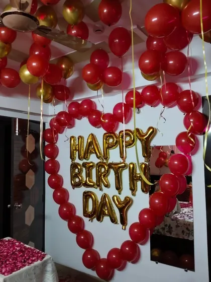 A romantic birthday surprise featuring a large heart made of red balloons on the wall. The 'Happy Birthday' foil letters are placed inside the heart, making it a central feature of the room decoration.