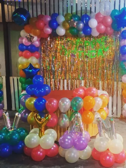 A colorful and playful setup for a first birthday celebration. The decoration includes multiple balloon pillars, an arch, and a decorated cake table.