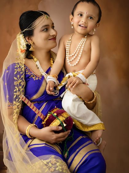 A loving gaze between mother and child. The baby holds a small matki, adding a playful element to this traditional Janmashtami portrait.