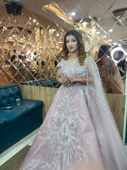 The client poses in our salon, showcasing her complete look against our signature mirrored wall. The soft lighting highlights the shimmer in her makeup and the sparkle of her gown.