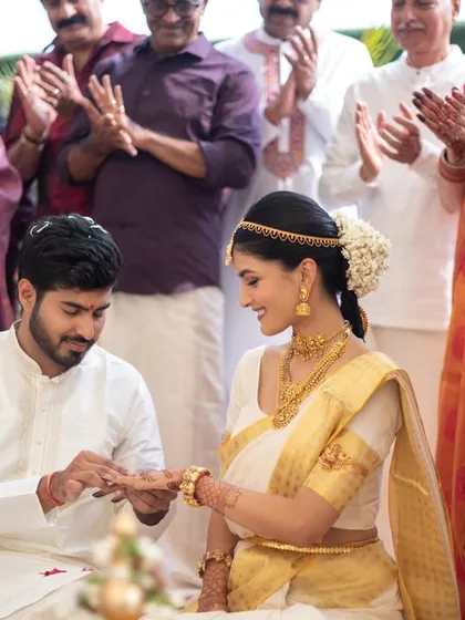 The ring exchange during a South Indian wedding ceremony, with family clapping in the background.