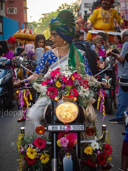 A woman in a traditional saree and ornate turban rides a motorcycle heavily decorated with flowers during the Gudi Padwa procession in Mumbai.