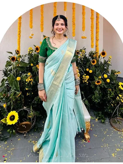 A bright and cheerful ensemble for a pre-wedding ceremony. The bride wears a lovely light blue saree with a contrasting emerald green blouse, featuring delicate embroidery on the sleeves and neckline.