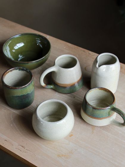 A beautiful selection of student pieces from the Apr-May cohort, featuring a lovely range of green and cream glazes on mugs, bowls, and a pitcher.