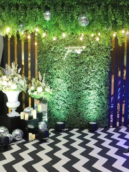 A modern photo booth setup with a lush green wall, a chevron-patterned floor, and artistic mannequins wrapped in neon lights, perfect for a contemporary event.