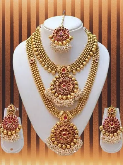 This complete bridal jewelry set is perfect for your big day. It includes two layered necklaces with red stone and pearl details, matching earrings, and a maang tikka to finish the look, all available for rent in Bangalore.