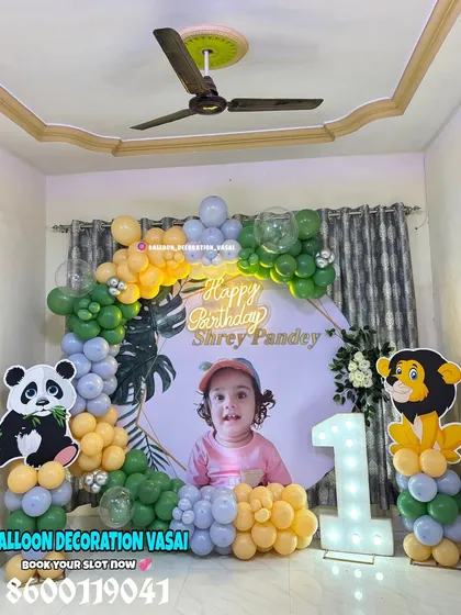 Shrey's first birthday with a gentle jungle animal theme. This home setup includes a custom photo backdrop, panda and lion cutouts, and a balloon arch in green, yellow, and grey.