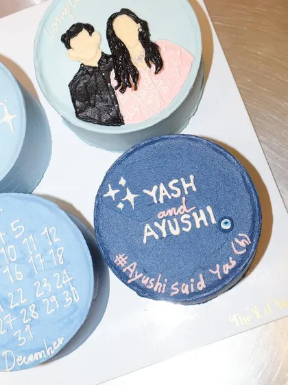 A close-up of a personalized engagement bento cake, part of a set celebrating a couple's big news. We love the evil eye detail for good luck.