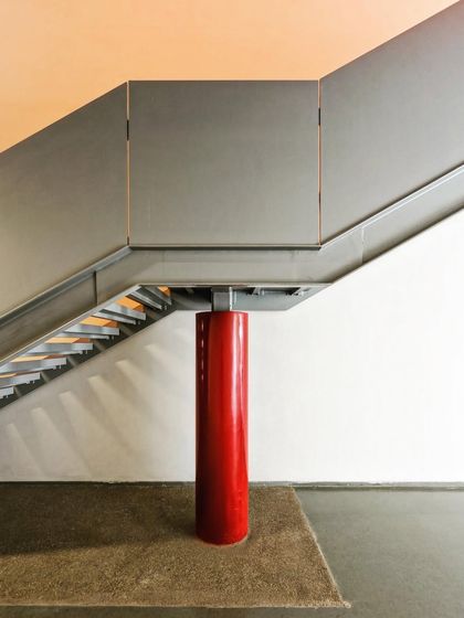 A detail of a staircase where a single, bold red column provides structural support. This expressive use of color and form turns a functional necessity into a striking architectural feature.
