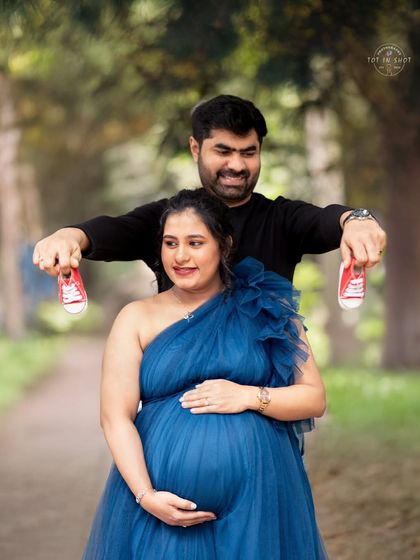 A fun and playful outdoor shot, with the dad-to-be holding up a pair of tiny red baby shoes.