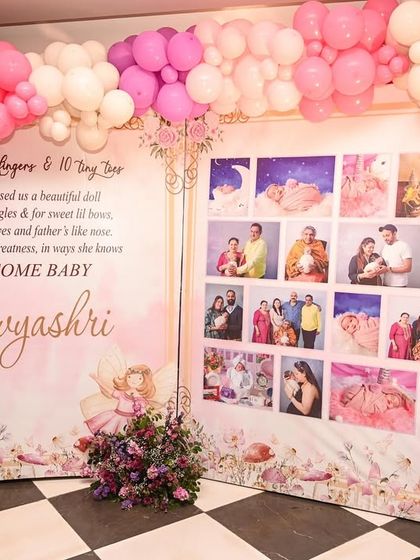A personalized photo wall surrounded by a pink and purple balloon arch. This display shares the family's journey and welcomes the new baby with a heartfelt poem.