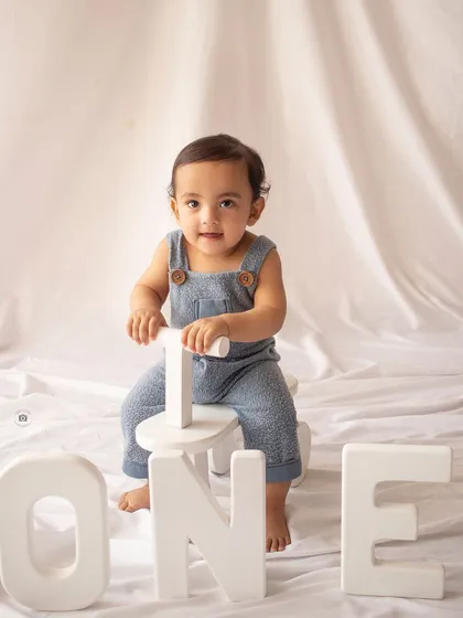 A classic first birthday portrait with a baby boy on a tricycle and "ONE" letters.