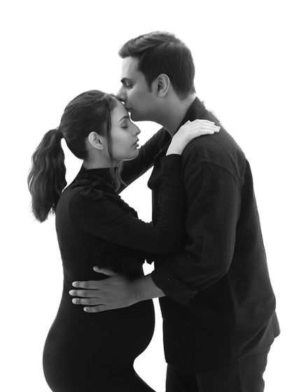 A timeless black and white portrait of the couple. His gentle kiss on her forehead and their simple, coordinated outfits create a classic and loving image.