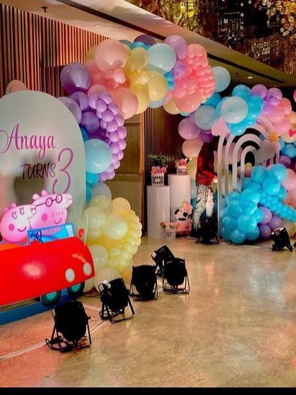 An entrance setup for Anaya's 3rd birthday Peppa Pig party, with a large balloon arch and a fun cutout of the Peppa Pig family in their red car.