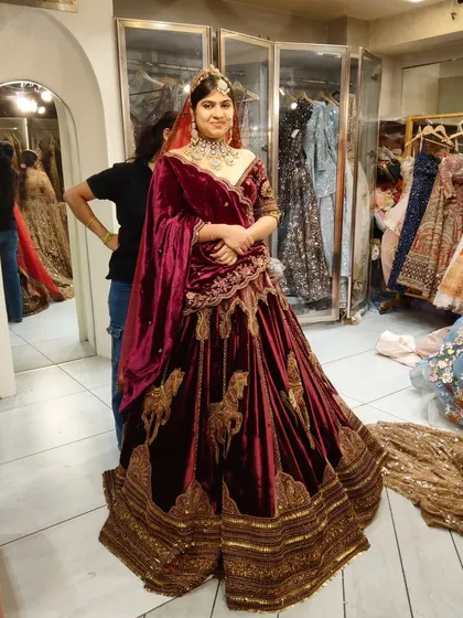 A bride looking regal in a deep maroon velvet lehenga. The rich fabric and gold zardozi work make it an ideal choice for a winter wedding.