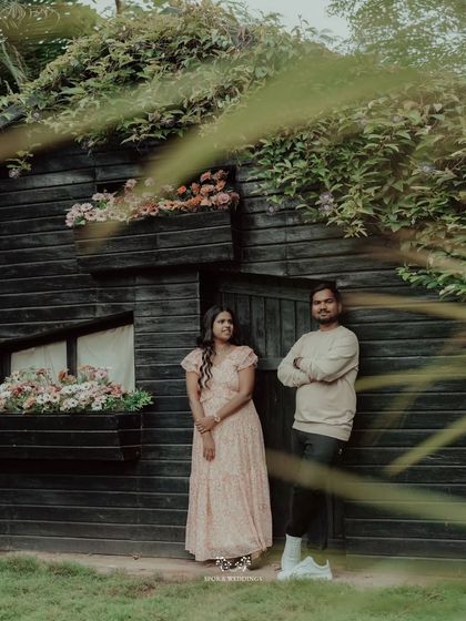 The couple posing in front of a charming, rustic black cabin with flower boxes.