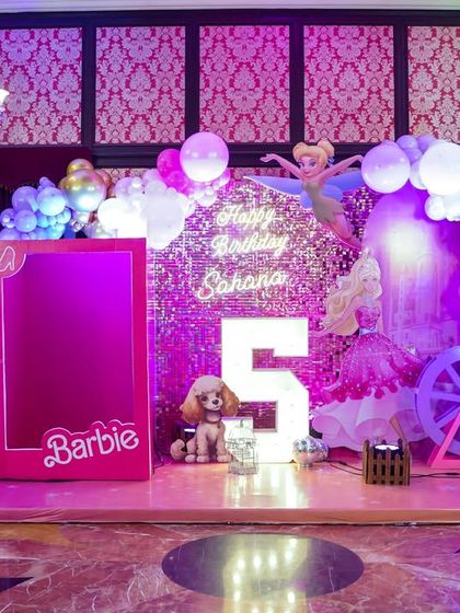 A glamorous Barbie-themed stage with a sparkling pink backdrop, a life-sized Barbie box for photos, and elegant lighting for a chic and stylish party.