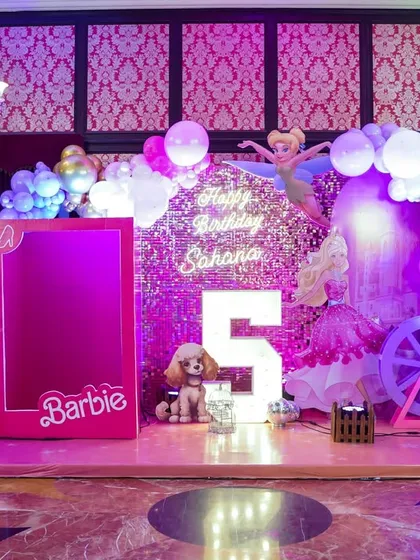 A glamorous Barbie-themed stage with a sparkling pink backdrop, a life-sized Barbie box for photos, and elegant lighting for a chic and stylish party.