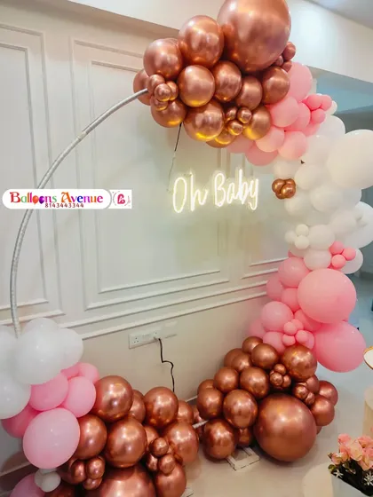 A close-up of a baby shower balloon arch in rose gold, pink, and white, with an 'Oh Baby' neon sign.