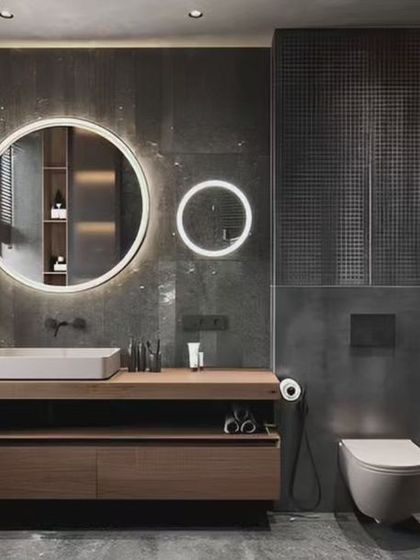 A bold, industrial-style bathroom with dark textured walls and twin backlit circular mirrors. The long wooden vanity provides ample counter space and storage.