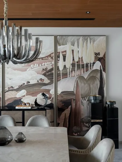 The dining area is defined by a large, expressive triptych artwork and a modern chandelier. The design creates an elegant setting for formal meals.