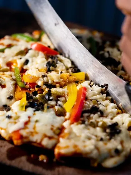 It's time to eat pizza and relax. A freshly baked pizza being sliced, ready to be served hot to guests at our live pizza counter.