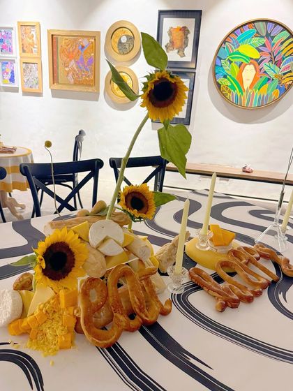 The word "Eat" crafted from pretzels stands tall among an arrangement of cheese, bread, and sunflowers. This tablescape was designed to be both a beautiful centerpiece and a delicious grazing board.