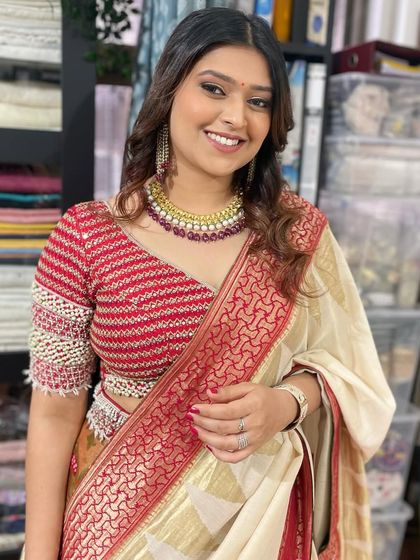 A classic look for a traditional ceremony, featuring soft curls and makeup that highlights her features. The red and cream saree is complemented by a warm, glowing makeup palette.