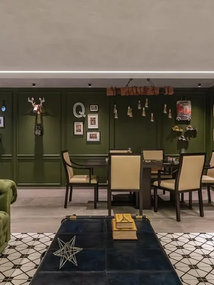 The entertainment room is designed for fun and relaxation. It features a sleek poker table, an emerald-green Chesterfield sofa, and unique decor like designer trunks and a transformer figurine.