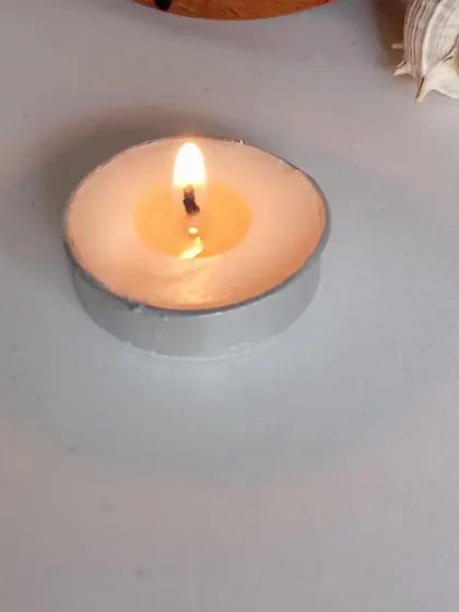 A single, lit tealight on a clean white surface. Sometimes the simplest things are the most beautiful, creating a peaceful retreat with just a small flame.