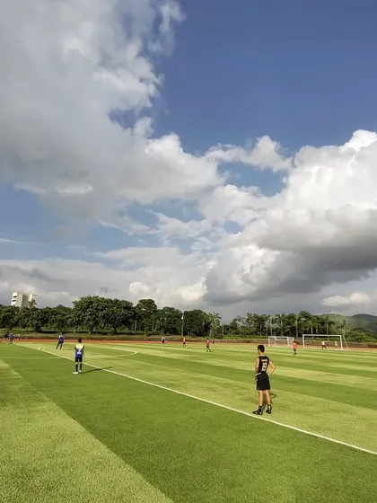 A stunning wide-angle shot of our players training on the academy pitch under a beautiful blue sky with scattered clouds. This is the dream environment for any aspiring young footballer.