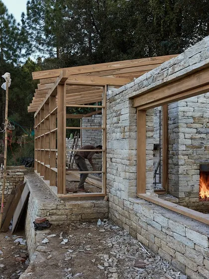 A fire burns in the hearth of a stone fireplace, with the timber framing of the house visible above. This image evokes the sense of warmth, shelter, and comfort that we strive to create in our homes.