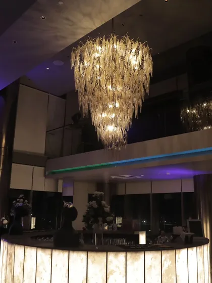 A magnificent, multi-tiered leaf-motif chandelier serves as a stunning centerpiece over the bar at a modern cocktail party, adding a touch of unique artistry to the space.