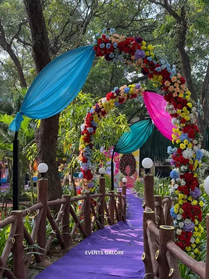 A colourful floral archway over a purple carpeted bridge. This pathway was designed to lead guests into the main carnival area, building anticipation with every step.