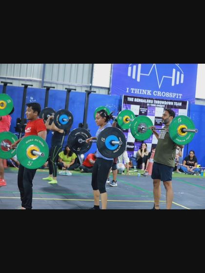 A line of athletes holding barbells in the front rack position, waiting for the signal to begin their synchronized squats.