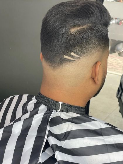 A back view of a pompadour with a high fade, featuring a subtle two-line design etched into the taper.