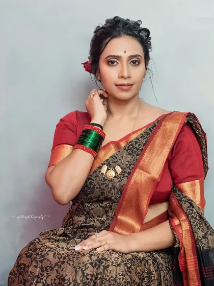 This seated portrait has a relaxed and natural feel. The red flower in her hair adds a pop of color that complements the red border of her saree.
