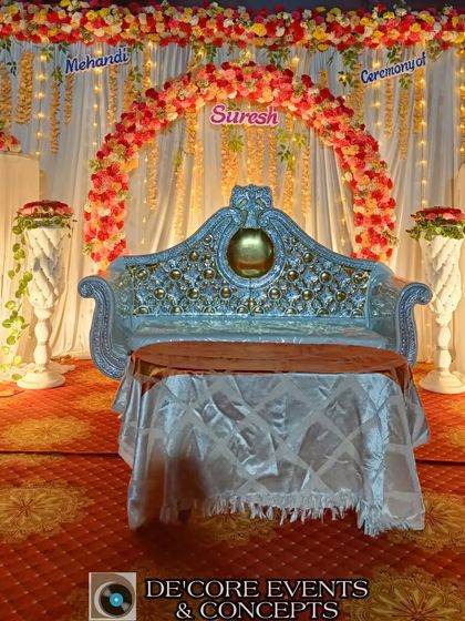 A classic Mehendi ceremony stage with a floral arch and traditional draping. The ornate silver sofa adds a touch of royalty to this colorful and festive setup.
