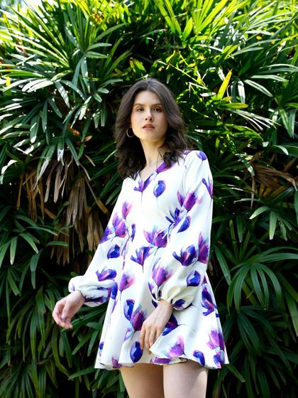 A model in a breezy, floral print mini dress with balloon sleeves. The movement in her pose and the sunny backdrop perfectly capture the carefree spirit of summer.