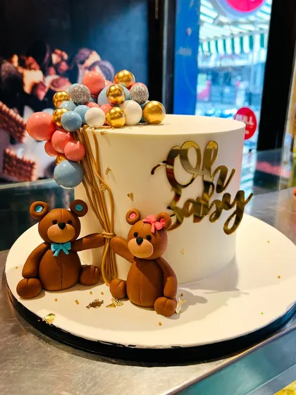 An "Oh Baby" shower cake with two cute teddy bears holding a bouquet of balloons.