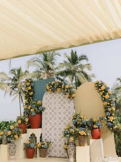The main seating area for the couple at the Mediterranean Haldi, featuring rattan chairs and a backdrop of patterned and solid-colored panels.