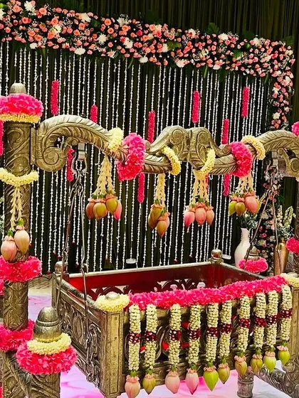 A beautiful cradle decorated with jasmine and pink flower garlands, set against a backdrop of hanging floral strings for a baby shower.