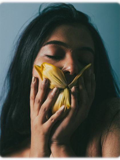 A mirror of shot 68, this time with closed eyes, suggesting a more internal, dreamy state. The hands cradling the flower and face create a sense of comfort and protection.
