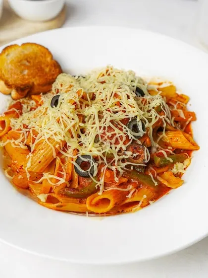 Penne arrabbiata in a rich red sauce, generously topped with cheese and served with garlic toast on a clean white plate.