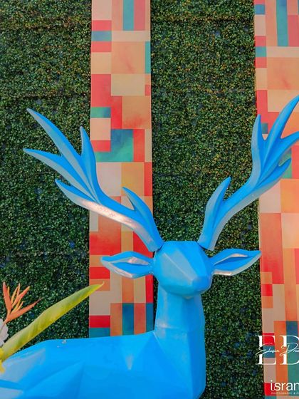 A geometric blue deer sculpture stands against a backdrop of a green wall and colorful patterned panels. This element showcases the blend of modern art and playful fantasy that defined the event's decor.