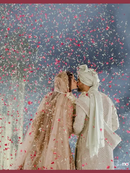 A shower of rose petals creates a magical, celebratory moment for the couple. This image captures the peak of emotion, a kiss that feels both epic and deeply intimate, embodying the spirit of a grand Indian wedding.